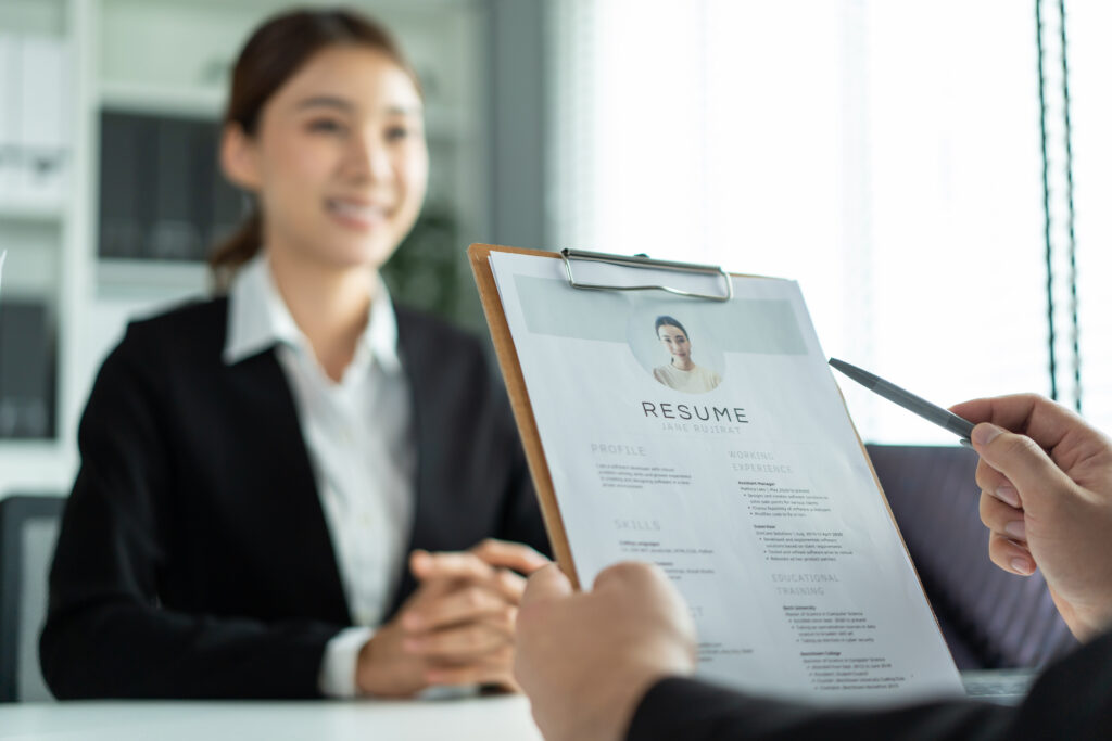 A young woman sitting across the desk from a hiring manager who’s reviewing her resume.