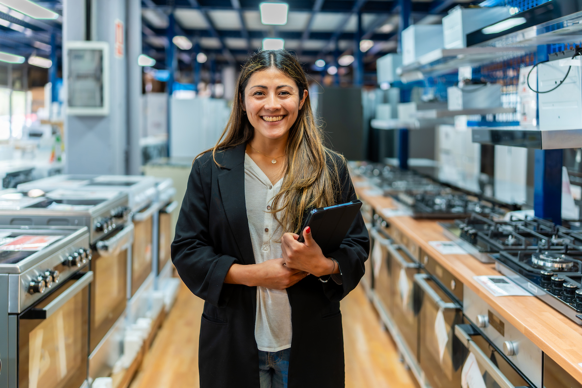 A business professional standing in the middle of an appliance store showroom with a tablet in hand